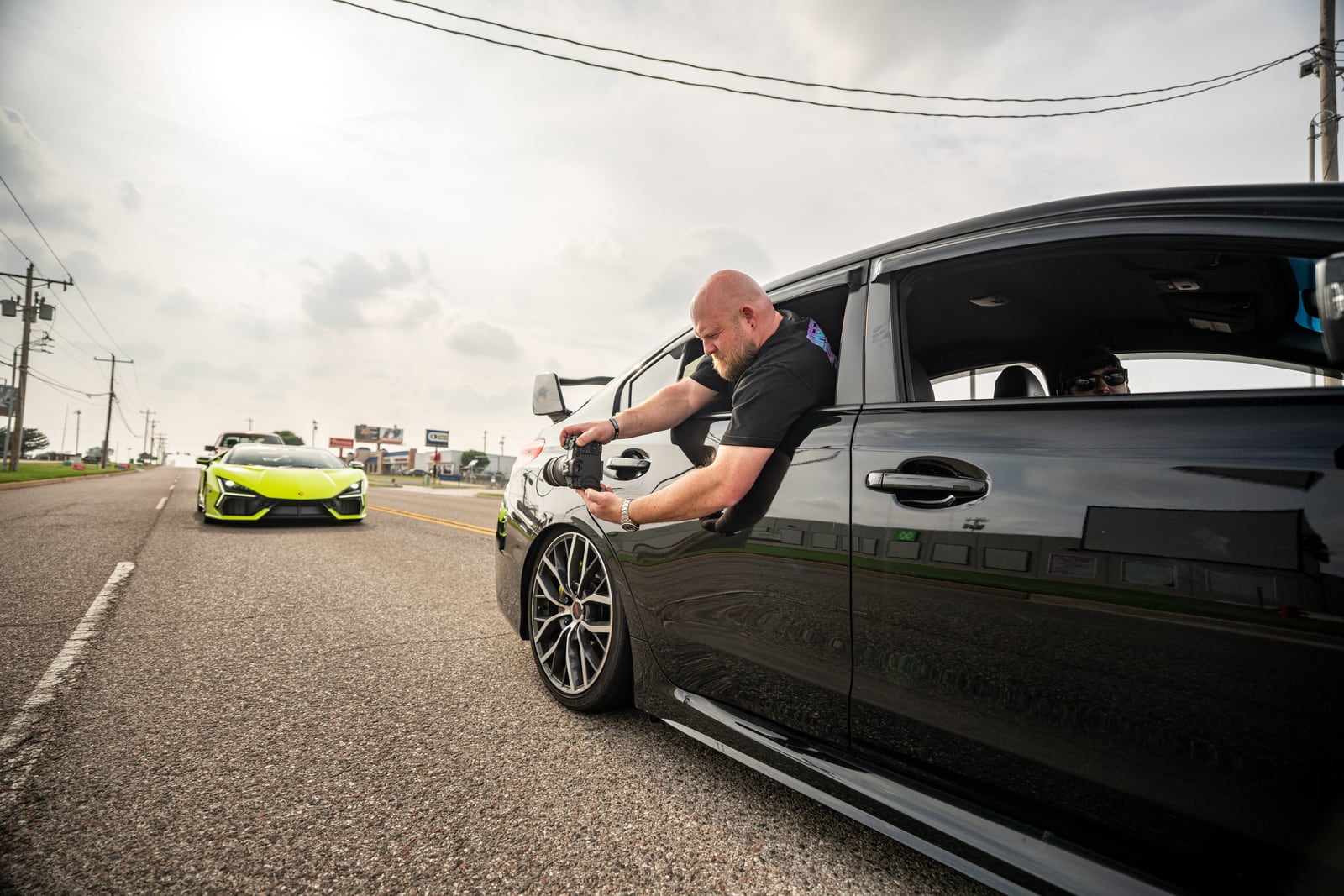 A photographer leans out of a rolling car to shoot the memorial cruise.